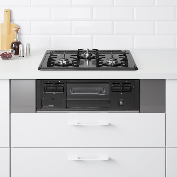 Modern kitchen with black gas stovetop and built-in oven. White cabinets. Small accessories on the left. Clean, spacious design.