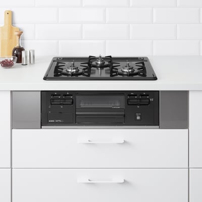 Modern kitchen with black gas stovetop and built-in oven. White cabinets. Small accessories on the left. Clean, spacious design.