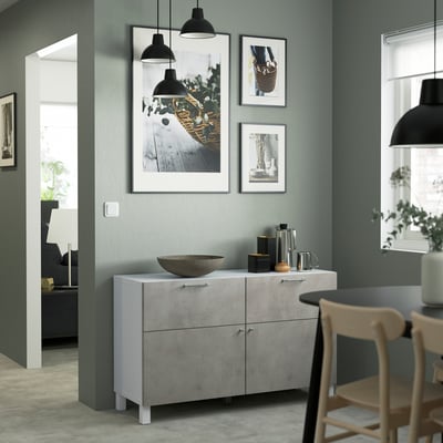 Modern living room with BESTÅ grey sideboard, lamps, & chairs around a dark table. Muted green walls & light flooring.