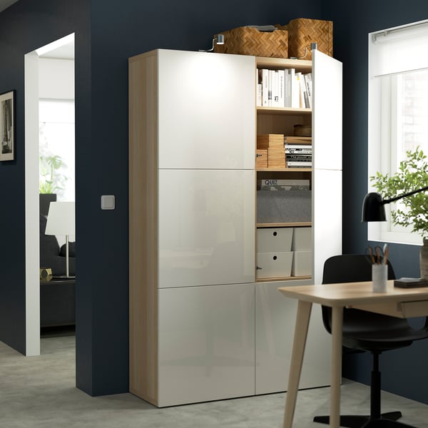 A modern white storage unit with open and closed sections, displaying books, boxes, and a lamp. It includes shelves and drawers for organised storage.