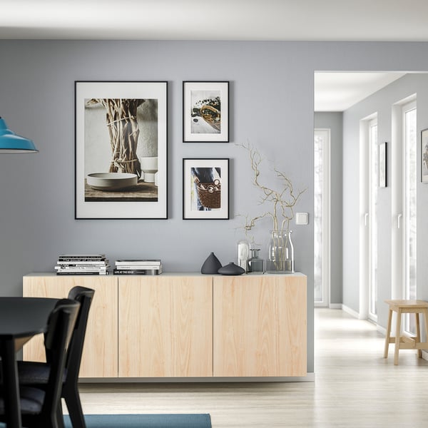 Modern living room with light wood BESTÅ cabinet, grey walls, three framed pictures, black and glass vases, and bare branches in a vase.