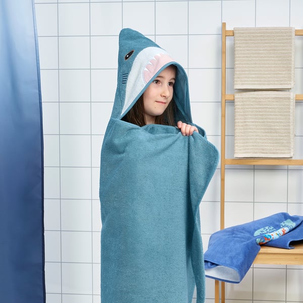 A child wraps in a blue shark towel with a hood, showcasing soft, absorbent cotton for warmth and drying after a bath.