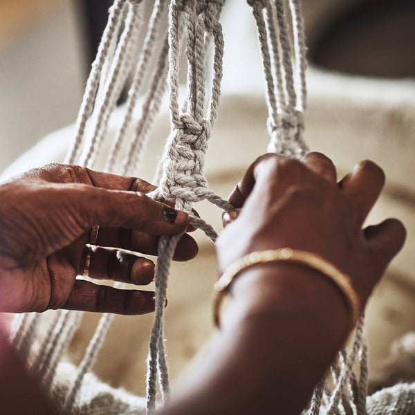 Two hands skillfully braid grey cotton strings, crafting a BOTANISK product.
