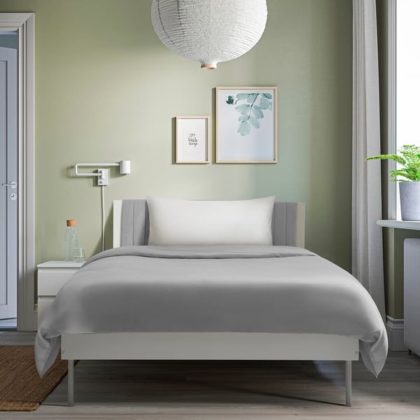 Modern bedroom with BRUKSVARA bed, soft headboard, ample storage. White bed, grey & white bedside table and door, two pictures, hanging lamp.