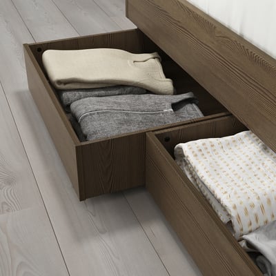 Wooden storage drawer, filled with folded blankets and sheets, slides under bed on castors.