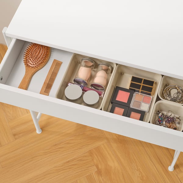 White dressing table drawer open, showing organised compartments with makeup brushes, makeup palettes, and jewellery.