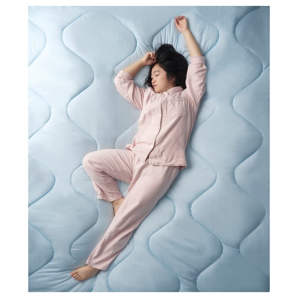 Image a girl in pink pyjamas lying on a blue wavy-patterned mattress, showcasing the BRUKSVARA duvet.