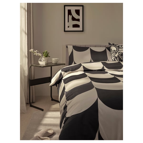 Modern bedroom with black and white bedding, monochrome artwork, and a black side table with a small plant and cup.