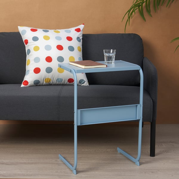 Small blue side table holding glass, book beside dark grey sofa with colourful dotted pillow.