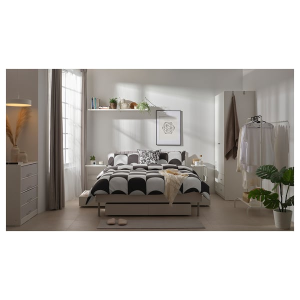 Contemporary bedroom with white decor, geometric bedding, hanging plants, and minimalist furniture.
