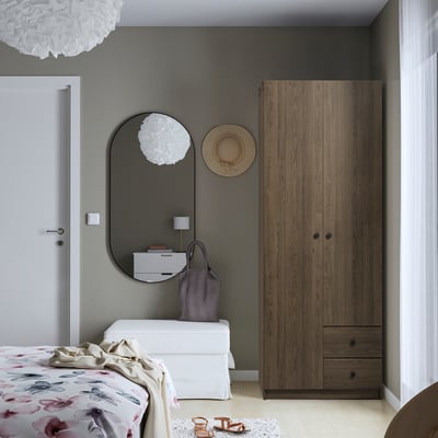 Illuminated bedroom with large wooden wardrobe, round mirror, white drawers, and floral bedding.