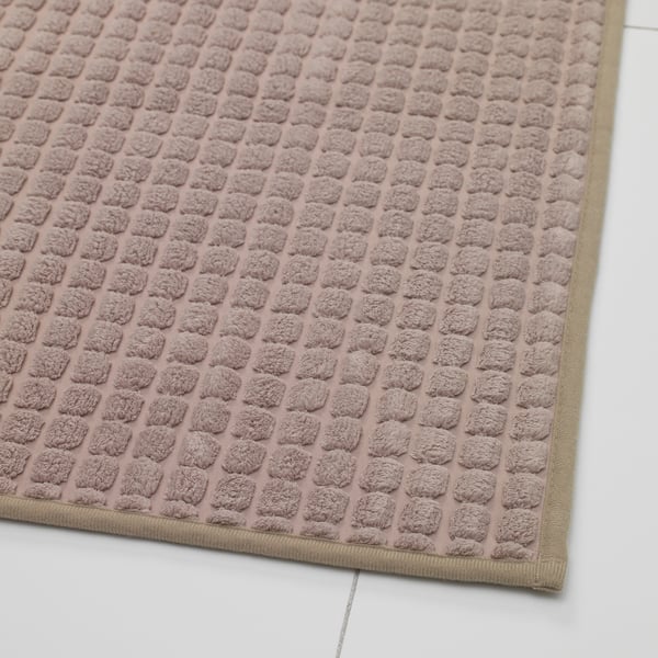 Textured pinkish rug with non-slip backing, laid flat on a white surface.