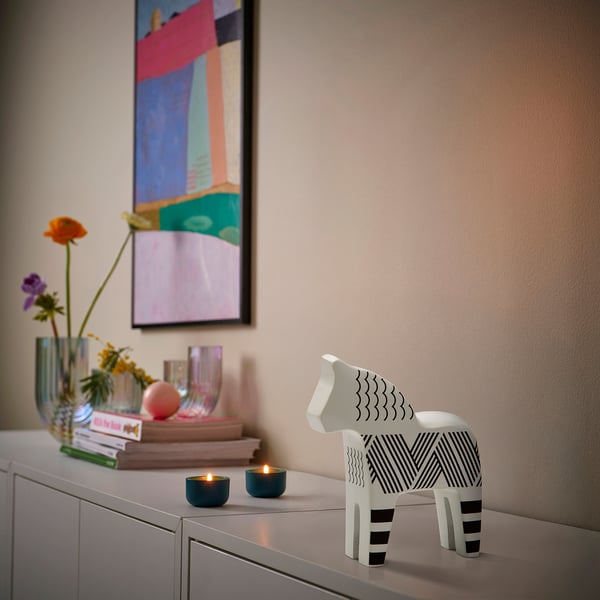 Wooden horse figurine with black stripes on shelf beside candles, vases, and books. Abstract painting above.