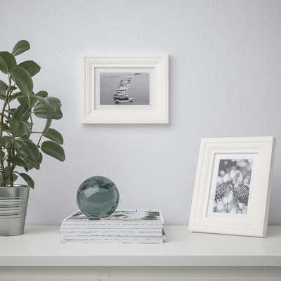 Wall & shelf with frames: boat, butterfly. Shelf has plant, books, sphere.