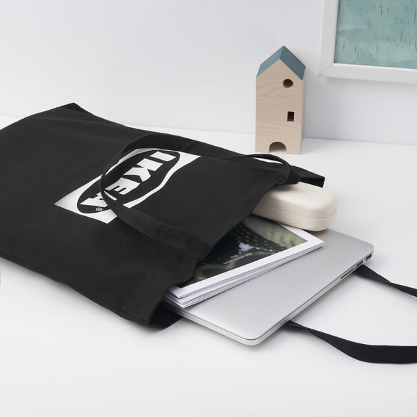 Black ikea EFTERTRÄDA tote bag holding a laptop and case, placed beside a small wooden house decoration.
