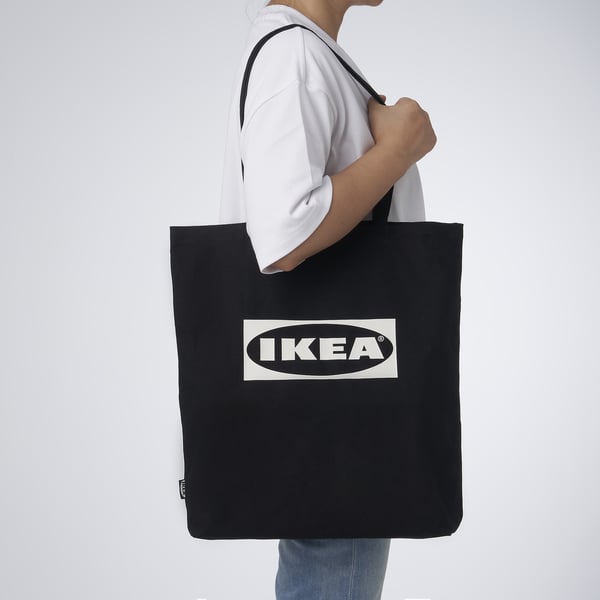 Person carrying black IKEA tote bag over shoulder. Bag has inner pockets for organising items.