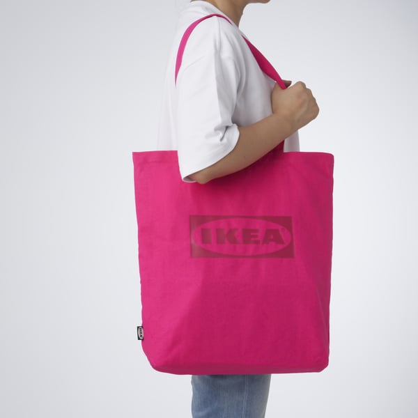 Person carrying bright pink ikea tote bag, designed for shopping, with inner pockets for small items, perfect for various outings.
