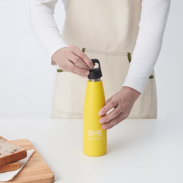 Person holding yellow ikea vacuum flask, demonstrating leak-proof lid.