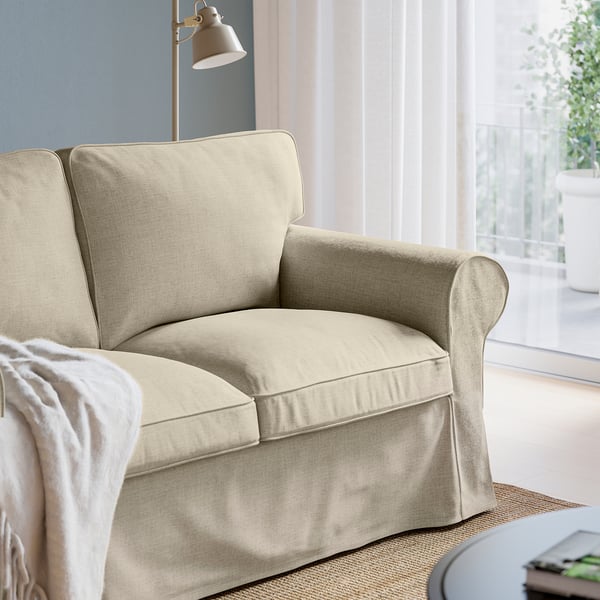 Comfortable beige EKTORP chair with thick cushions, near window with light-colored curtains.