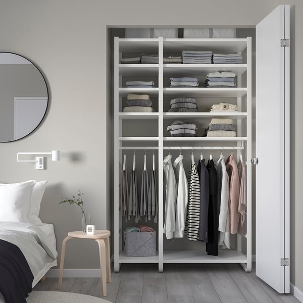 Modern white ELVARLI storage system beside bed, with shelves, hanging rack, mirror, desk, and plant.