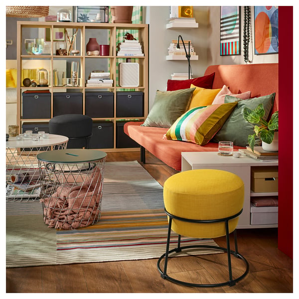 Bright living space with orange sofa, colourful pillows, yellow stool, and wooden shelves filled with books and decor.