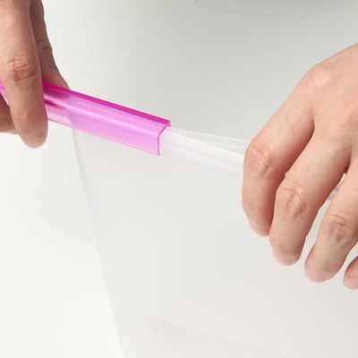Hands opening a FILFISK resealable bag, suitable for food storage and microwaving.
