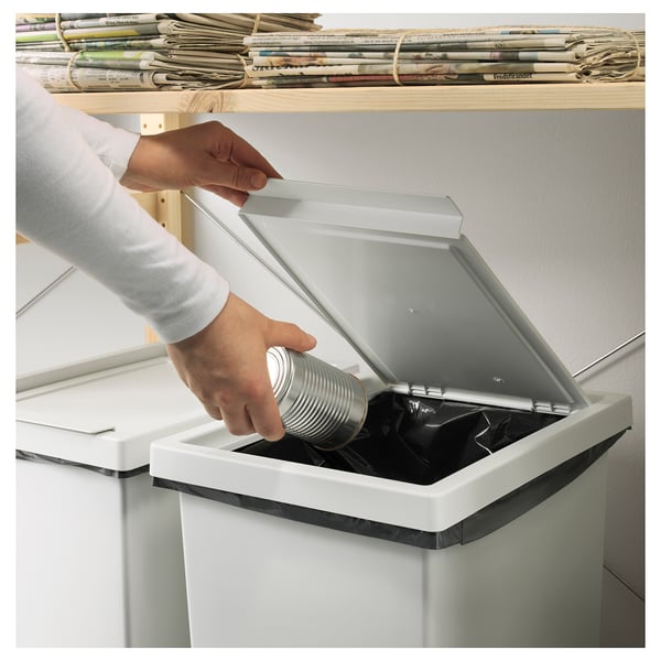 Person disposing a can into a white recycling bin with a lid.