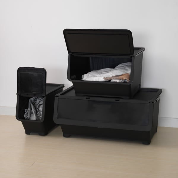 Black storage boxes with wheels. One is empty, another shows clothes inside, and a third is stacked with a lid. Ideal for organising and moving items.