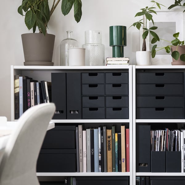 Bookshelf with black FJÄDERHARV magazine holders and assorted books, vases, plants, and a green lamp.