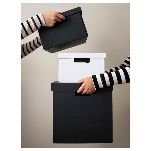 Person holding black FJÄDERHARV storage box, stacking with another.
