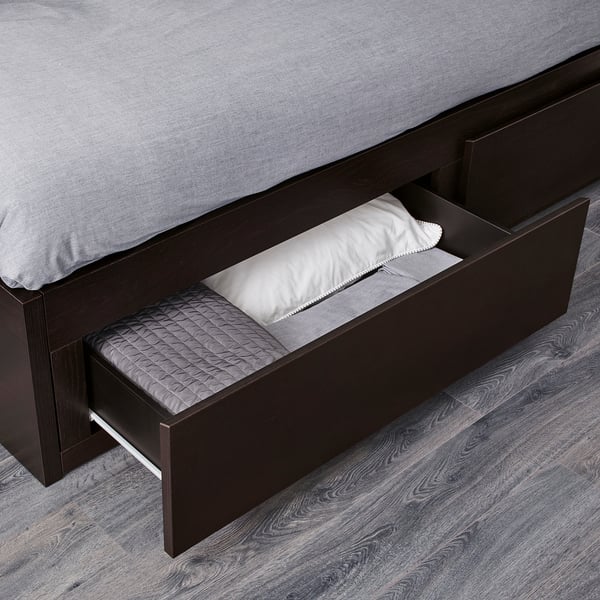 Dark wood daybed with open drawer revealing folded linens, showcasing storage function.