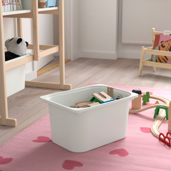Playroom with light pink rug, white storage bin holding wooden toys. Wooden bookshelf, toy chair, and track nearby.