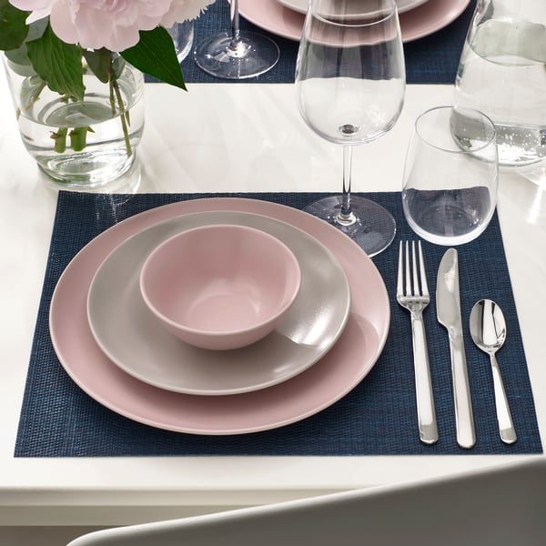 Table setting with pink plates, bowls, and silverware on blue place mats. Wine and water glasses included.