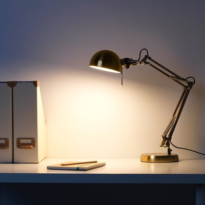 A stylish, adjustable work lamp in gold on a desk, casting directional light.