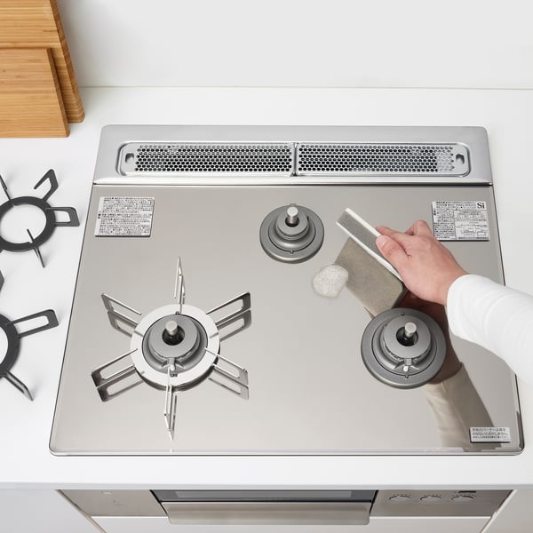 Person cleaning modern gas stove with three burners and fish grill.