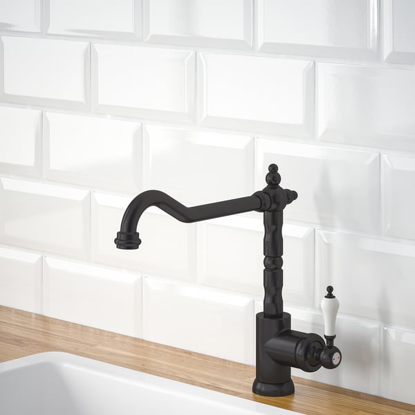 Black kitchen tap with a curved spout and side handle, set against white tiles and a wooden countertop. It aids in water and energy efficiency.
