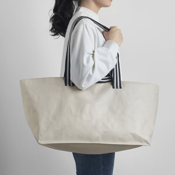 A person holding a large, beige tote bag with black and white striped straps. The bag appears spacious and easy to carry.
