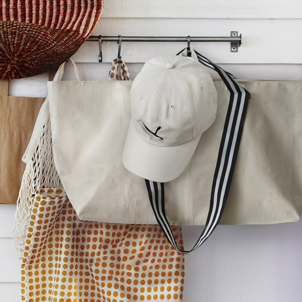 White cap and tote bags on wall rod. Cap: light with black logo. Bags: beige stripes, red polka dots. Neat storage.