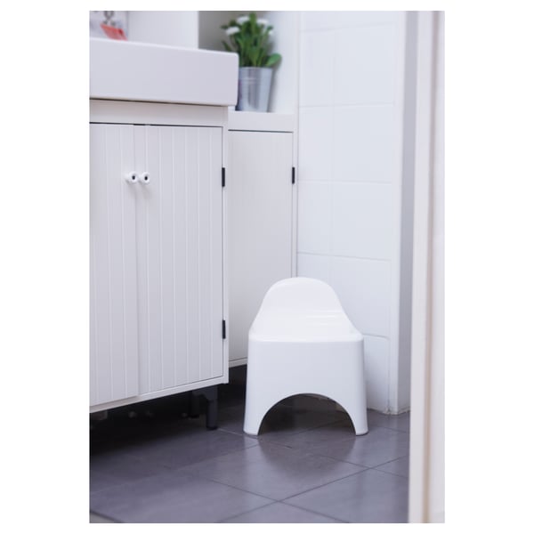 Bathroom stool with backrest against white cabinet, plant on top.