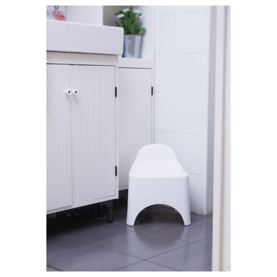 Bathroom stool with backrest against white cabinet, plant on top.
