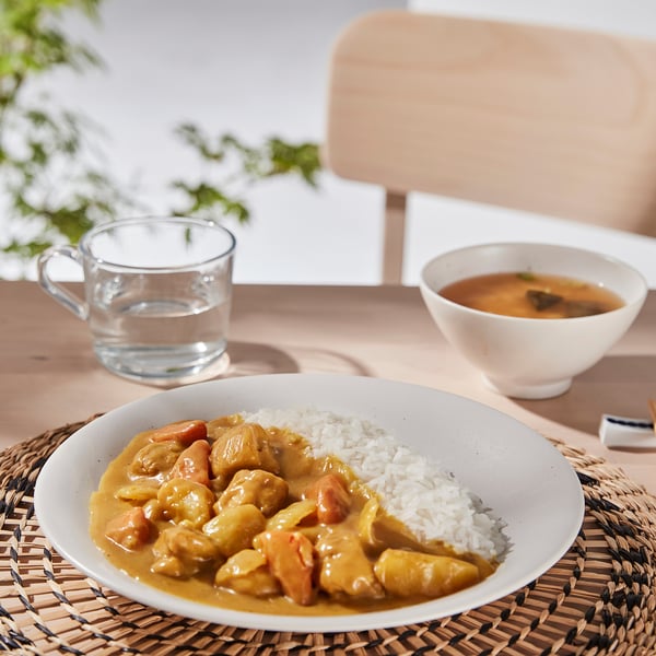 A bowl of curry and rice on a table with a cup of tea and a soup bowl, showcasing the HARMYNTA stacked dinnerware for easy serving and storage.