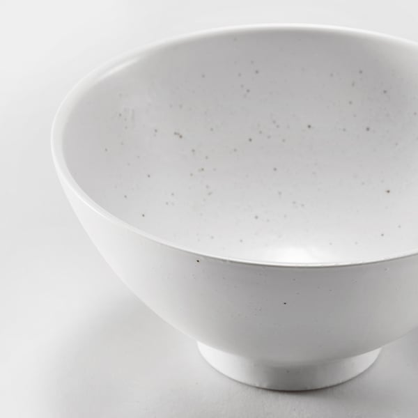 Elegant white porcelain bowl, speckled glaze, smooth edges, refined finish.
