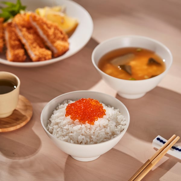 A table with bowls of rice topped with red caviar, miso soup, breaded meat, and a cup of tea. Chopsticks are placed beside the bowl.