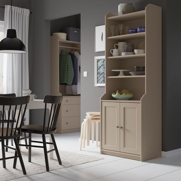 Modern kitchen with light brown HAUGA cabinet, glassware, and black chairs.