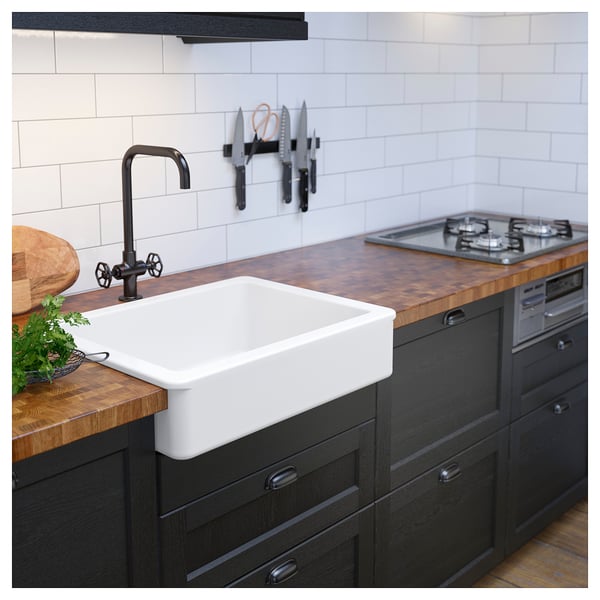 Modern kitchen with white sink, dark tap, wooden counter, dark cabinets, knife magnet, and gas range.