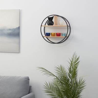 Modern black shelf with colourful cups, beside plant & painting, above couch.
