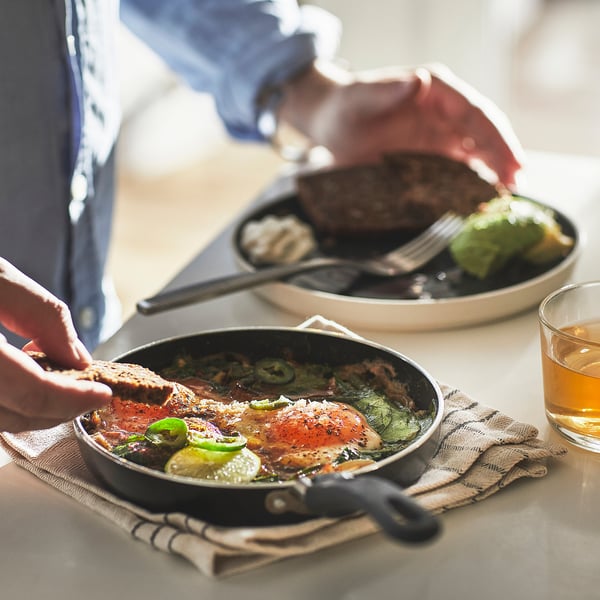 Person serving meal in small non-stick pan on table with drink.