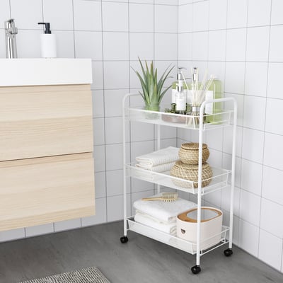 Bathroom storage trolley HORNAVAN, white, metal & plastic, three-tiered. Fits neatly beside wooden vanity, holds towels, plants, & toiletries.