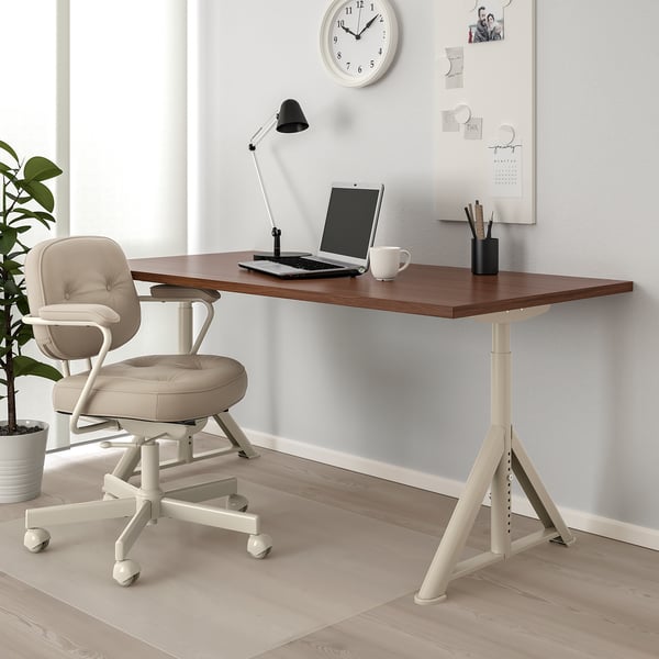 IDÅSEN desk in minimalist office with wooden top, off-white legs, cable management, and a beige chair underneath. Clock and plant nearby.