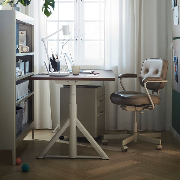 Home office setup with IDÅSEN desk, leather chair, laptop, lamp, and bookshelf.